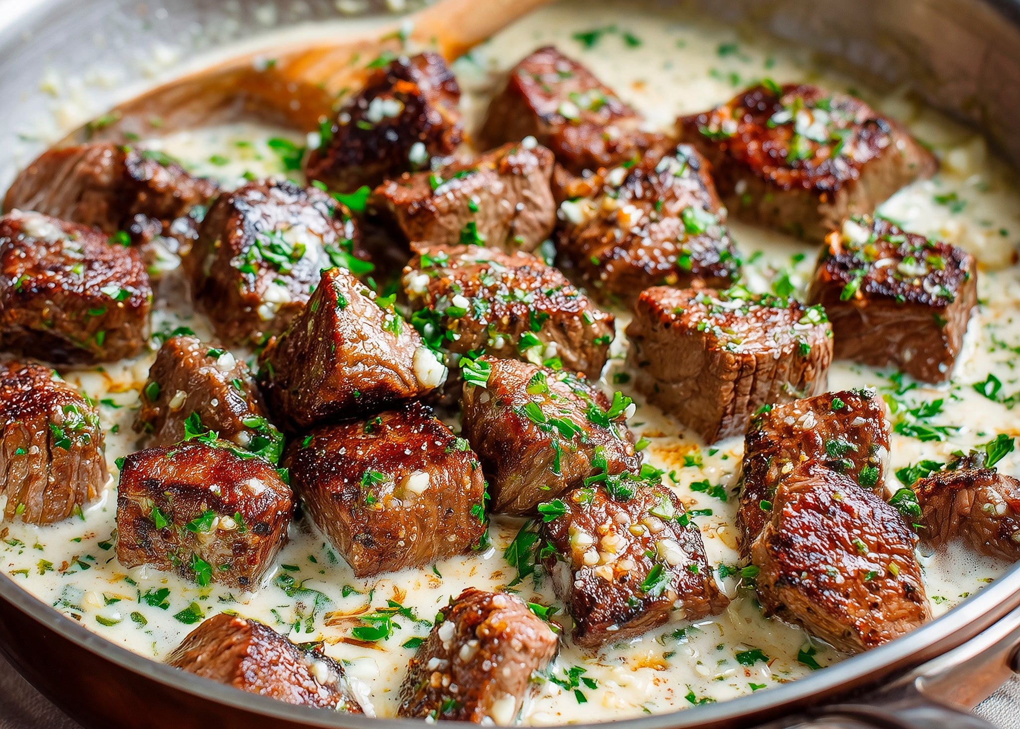 Bison Steak Bites, grass-fed and finished Pan-seared steak bites cooked in a creamy garlic butter sauce, garnished with chopped herbs in a skillet 