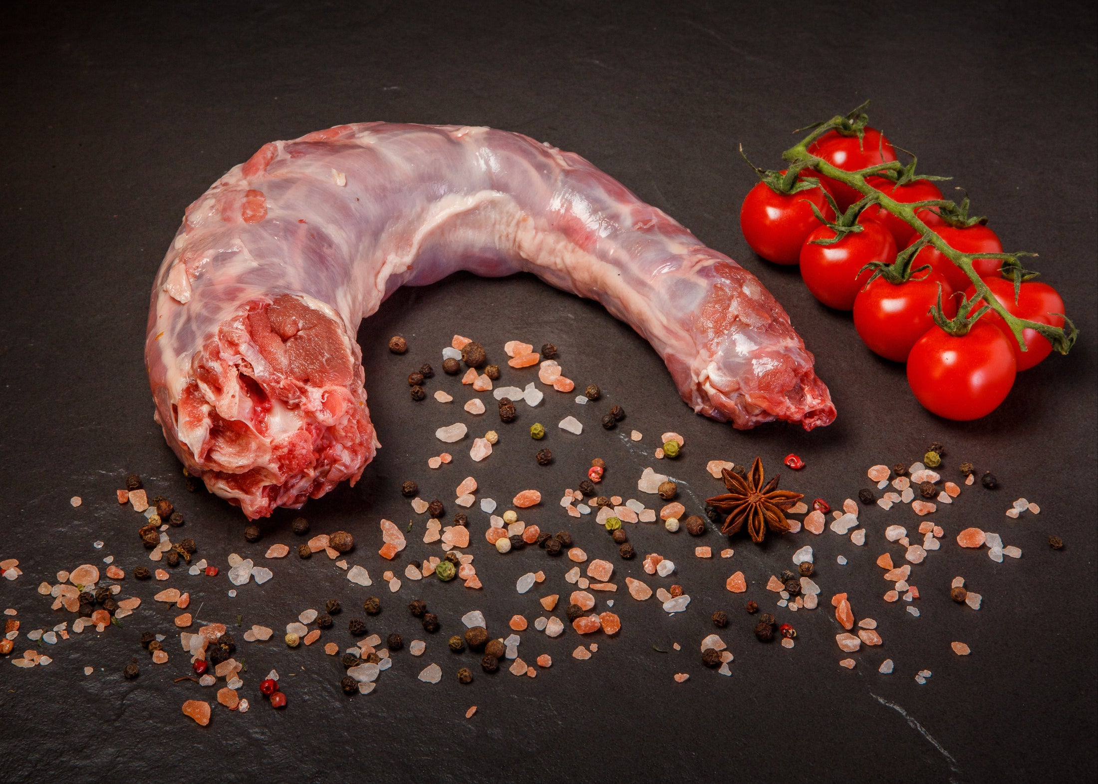 Raw duck neck with cherry tomatoes, peppercorns, and pink salt on a dark background for recipe, food, and pet food.